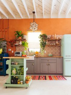 a kitchen with orange walls and lots of potted plants on the counter top next to a blue refrigerator