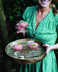 a woman in a green dress holding a tray with desserts and drinks on it