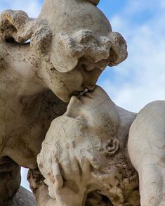 two statues are touching each other in front of a blue sky with clouds behind them