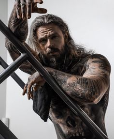 a man with long hair and tattoos on his body is standing next to some stairs