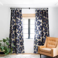 a living room with blue and yellow flowers on the curtains, a brown chair and potted plant