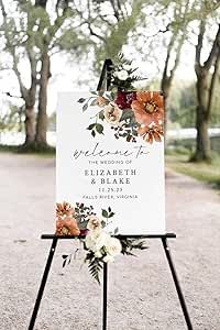 a wedding sign with flowers on it sitting in the middle of a road next to trees