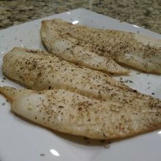 two fish fillets on a white plate with seasoning sprinkled on them