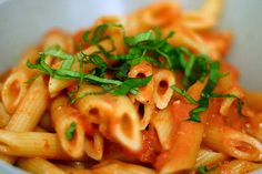 a white bowl filled with pasta covered in sauce and garnished with parsley