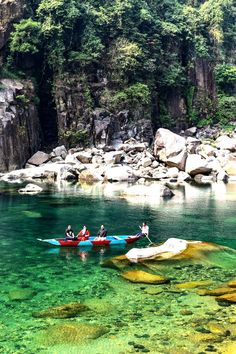 two canoes with people in the water near some rocks and green trees on either side