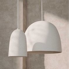 two white lamps hanging from a ceiling next to a wall with concrete walls in the background