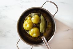 a pot filled with pickles on top of a white marble countertop next to a metal spoon