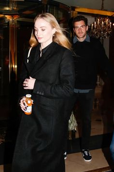 a woman in black coat and jeans walking down stairs next to a man with his arm around her