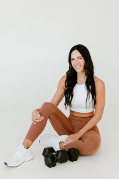 a woman sitting on the ground with her legs crossed and wearing brown leggings