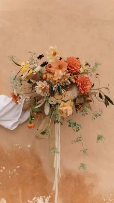 a bridal bouquet with peach, yellow and white flowers is tied to a wall