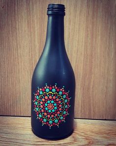 a black bottle with colorful dots on it sitting on top of a wooden table next to a wall