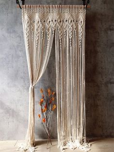 a white curtain hanging on the side of a wall next to a vase with flowers