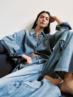 a woman sitting on top of a couch wearing blue denims and jeans with her legs crossed