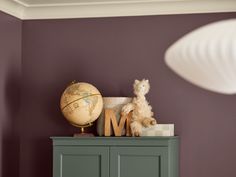 a teddy bear sitting on top of a green cabinet next to a lamp and globe