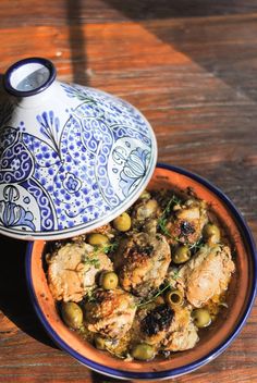 a blue and white bowl filled with food on top of a wooden table next to a vase