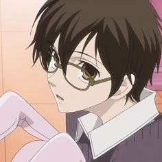 an anime character with glasses sitting in front of a tile wall and looking off to the side