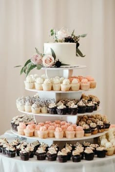 a tiered cake with cupcakes and flowers on the top is surrounded by other desserts