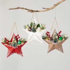 three star ornaments hanging from a branch with pine cones and berries on them, decorated with greenery