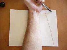 a person holding a pen and writing on paper with a pencil in their left hand