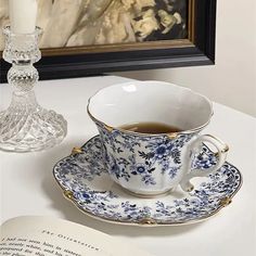 a tea cup and saucer sitting on top of a table next to an open book