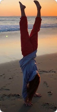 a person doing a handstand on the beach with their feet in the air