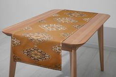 a wooden table topped with a brown and gold patterned table runner next to a white wall