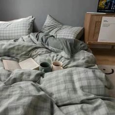 an unmade bed with a book, cup and mug sitting on top of it