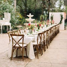 a long table is set up with white linens and wooden chairs for an outdoor dinner