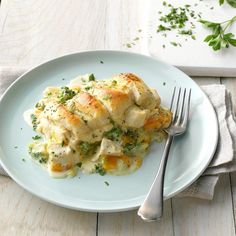 a white plate topped with chicken and dumplings next to a fork on top of a wooden table