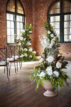 flowers are in a vase on the floor next to two chairs with windows behind them