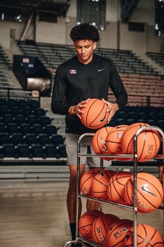 a young man holding a basketball in front of a cart full of orange basketballs