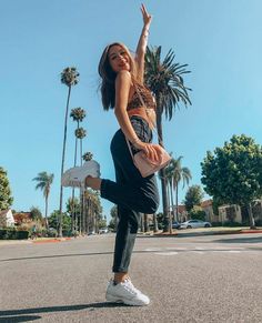 a woman standing in the middle of an empty street with palm trees and buildings behind her