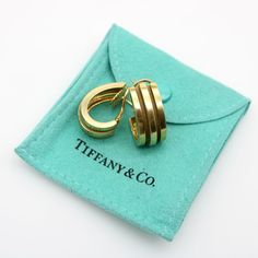 This is part of Chairish’s Fine Jewelry assortment.  These 18k gold vintage Tiffany & Co. earrings are from 1995. They are part of the iconic Tiffany & Co. Atlas collection, which featured designs inspired by the Roman numerals found on the Atlas clock. These deep ribbed hoop earrings have a high polish that alternates with matte gold within its recesses, creating a streamline look of three simple bands of gold. The design is fluid, clean, and modern and makes for a sophisticated pair of earring Tiffany Co Earrings, Tiffany Earrings, Vintage Tiffany, Simple Band, Maker’s Mark, Magic Ring, Loop Earrings, Expensive Jewelry, Tiffany And Co