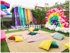 an outdoor party with balloons, pillows and blankets on the ground in front of a fence