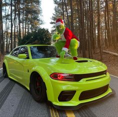 a person dressed as grinen riding on the hood of a green car in front of some trees