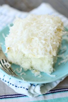 a piece of coconut cake on a blue plate with a fork and napkin next to it