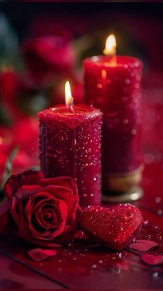 two red candles with hearts and roses on the table in front of them, one is lit