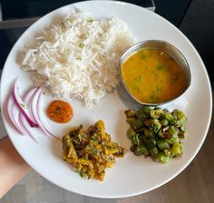 a white plate topped with rice and veggies next to a bowl of sauce