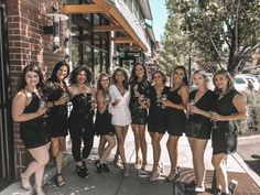 a group of women standing next to each other in front of a building holding wine glasses