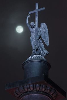 an angel statue holding a cross on top of a building with the moon in the background