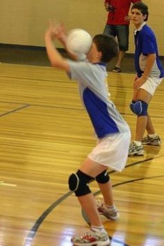 a young boy holding a white ball on top of a hard wood floor in a gym