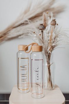 two clear glass bottles sitting on top of a wooden table next to dried plants and feathers