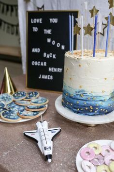 a birthday cake with stars on top and candles in the shape of an airplane sits next to other desserts