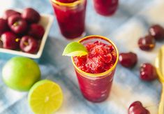 two glasses filled with fruit sitting on top of a table next to limes and cherries