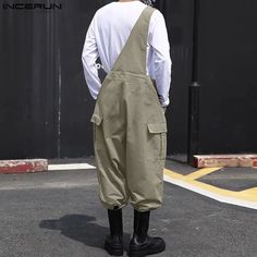 a man wearing overalls and black boots stands in front of a building with his back to the camera