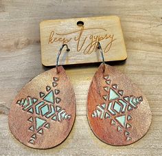 two wooden earrings with designs on them sitting next to a wood sign that says keep happy