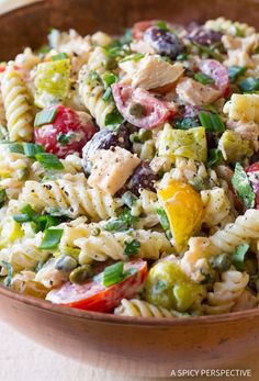 a pasta salad with chicken, olives, tomatoes and other vegetables in a wooden bowl