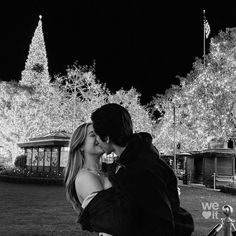 a man and woman kissing in front of christmas lights