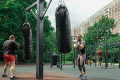 a man is practicing boxing in the park with punching gloves on his chest and other people behind him