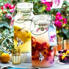 two mason jars filled with liquid sitting on top of a table next to fruit and flowers